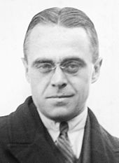 Black and white photo of a bespectacled man in suit and tie looking at the camera