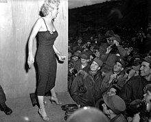 Marilyn Monroe poses as a crowd of soldiers photograph her