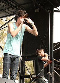 Two light-skinned men are seen singing into their microphones.