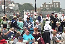 A photograph taken during the Broadstairs Dickens Festival of 2013. People are dressed as various Dickensian characters as part of the festival. Bleak House (formally Fort House) where Charles Dickens often stayed can be seen in the background.