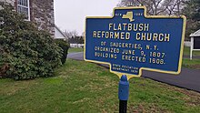 a picture of the marker, with the stone wall of the church behind it