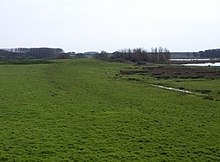 field with raised grass track leading to distant mound