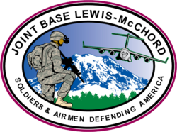 Arméfordon lastas ombord på en av flygvapnets C-17 Globemaster III vid Joint Base Lewis-McChord med Mount Rainier i bakgrunden samt basens emblem.