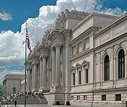 Facade of imposing building with Greek columns. Large colored banners hang from the building's top. A crowd of people is in front.