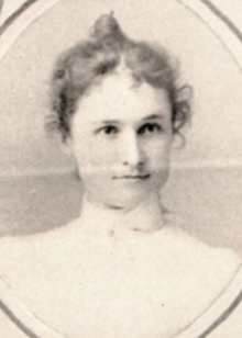 A white woman with hair in an updo, wearing a high-collared white blouse, in an oval frame