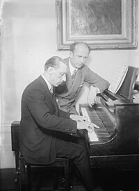 Black and White photo of Stravinsky playing an upright piano, Furtwangler sitting beside him studying the score