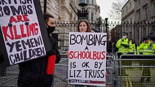 Two women at the Downing Street gates holding placards reading "British bombs are killing Yemeni children" and "Bombing a schoolbus is OK by Liz Truss #stopkillingyemenichildren".