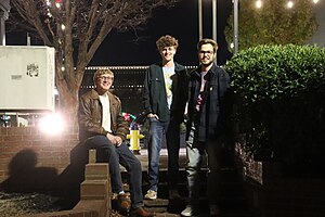 Three young men standing in front of a stairway in a downtown area.