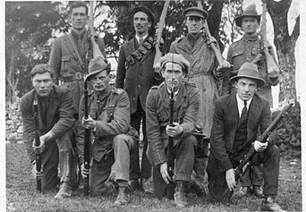 Eight Irish men holding rifles in a group photo from 1922. Brian Molloy is in the front row, third from the left, with a stern expression on his face.