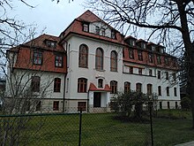 fünfstöckiges Haus, davor Wiese, ganz vorne: Zaun.