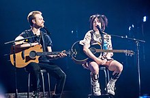 Billie Eilish and her brother onstage for a world tour, holding their acoustic guitars