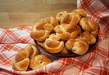 Tigela de madeira com pãezinhos de cardamomo recém-assados em uma toalha de linho xadrez. O pão de cardamomo é um pão doce, semelhante a um bolo, aromatizado com cardamomo e popular na Suécia. É preparado no forno ou em uma panela especial. A massa é feita com fermento, manteiga, leite, açúcar e cardamomo. Tiras são formadas a partir da massa, que são então trançadas. O pão é frequentemente coberto com nozes picadas e sorvete de baunilha. O método de cozimento com o forno leva cerca de duas horas. (definição 4 124 × 2 840)