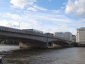 Wide bridge over water against a grey sky with tall buildings