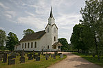 Foto einer weißen Holzkirche mit dunklem Dach. Im Vordergrund befindet sich ein Friedhof.