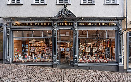 Livraria N.G.Elwert em Marburgo, Hesse, Alemanha. As lojas de vendas de livros podem variar em tamanho, oferecendo de várias centenas a vários milhares de títulos. Elas podem ser lojas de presença física em um prédio ou outra estrutura, ou lojas apenas na Internet ou uma combinação de ambas. As livrarias costumam vender outros impressos além de livros, como jornais, revistas e mapas. As faculdades e universidades costumam ter livrarias no campus que se concentram no fornecimento de livros didáticos e livros acadêmicos. Outro tipo comum de livraria é o sebo ou alfarrabista que compra e vende livros usados ​​e esgotados em uma variedade de condições. (definição 7 130 × 4 456)