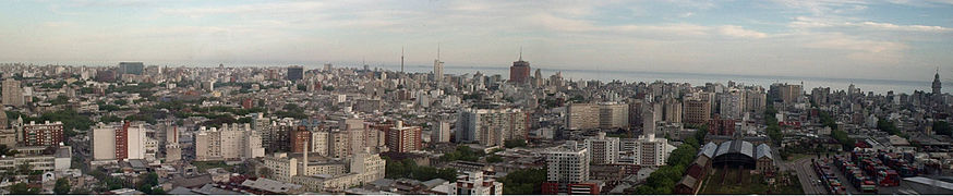 Foto Panorámica de los barrios Aguada, Centro y Cordón de Montevideo, tomada desde la torre de Antel. Se distingue el edificio de la intendencia de Montevideo (centro), el palacio Salvo (derecha) y la Estación Central General Artigas abajo a la derecha. Además, a su derecha se encuentra el Puerto de Montevideo que se ubica en la Bahía de Montevideo.