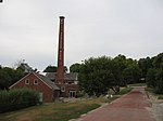 View of a red-brick path, with a red-bricked mill that has chimney stack built in its centre to the side of the path