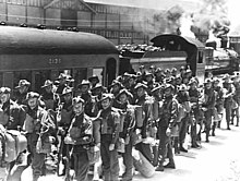 Soldiers in service dress uniform stand near a train