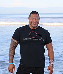 Tuaolo standing on a beach in a wetsuit