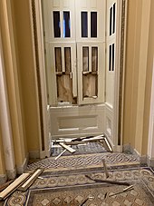 A photo taken from the inside of the Capitol building. Windows are broken, along with their wooden frames. They are boarded up.