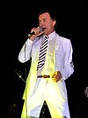 A man in a white tuxedo is facing left holding a microphone