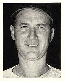 A close-up of a smiling man wearing a baseball jersey and cap