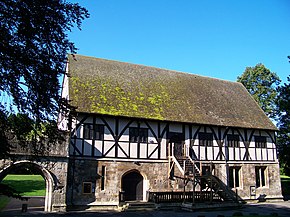 Two story building with half timber second floor built over the stone first floor. Wooden staircase goes to the entrance on the second floor.