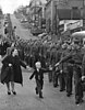 Soldiers marching down the street with a boy chasing his father