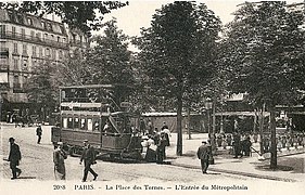 Photo légèrement sépia d'une place avec piétons, omnibus et entrée d'escalier ouvragée dans les arbres