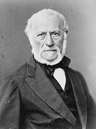 Portrait photographique d'un homme aux cheveux blancs, à la barbe blanche, vêtu d’une chemise, d’un veston, d’une veste et d’un nœud papillon