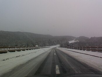 A snowy highway road that is icy and looking toward forests and mountains.