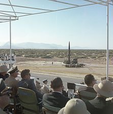 Förberedelse av vapentest av en Pershing I-robot på WSMR den 5 juni 1963. USA:s 35:e president John F. Kennedy (D) sitter höger om en uniformerad militär och har på sig solglasögon. Vänster om militären sitter USA:s 37:e vicepresident Lyndon B. Johnson med en tropikhjälm på huvudet. Militären som är "bakom" Kennedy är USA:s arméstabschef Earle Wheeler.