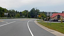 A broad stretch of curved paved road, with turn lanes and a double yellow line down the center, photographed from its side. At the right is a small building with a reddish cross-gabled roof; a sign on the road says it is the "Apple Barrel Café". In the front right are two black on white signs with the numbers "30" and "30A" on them