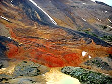 A windswept mountainside with red-orange rock