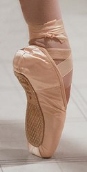 Una scarpa da punta, fissata al piede di una ballerina. La ballerina è en pointe, il che significa che tutto il peso del corpo è supportato dalla punta dei piedi completamente estesi.