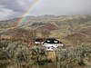 View of the James Cant Ranch, a large white three storey building with a black roof, set in a landscape of trees and grassland with a rainbow in the background