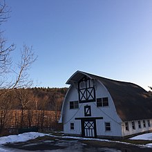 3 story barn with some snow on the ground, mountain in the background nd a cloudless sky