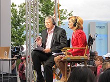 A man and a woman anchoring a newscast on an outdoor set
