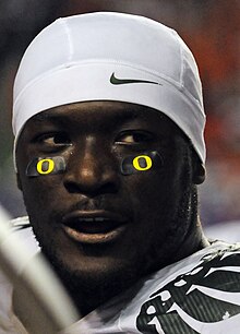 Portrait de LeGarrette Blount avec un bandana blanc et des stickers noirs avec le logo jaune d'Oregon sous ses yeux.