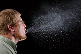 Photograph of a man sneezing, with droplets dispersing widely