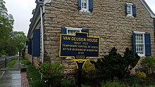 a picture of the marker, with the old stone building behind it, showing that the stone house is right next to the road