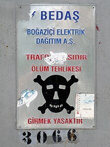 Old metal sign with black skull and crossbones and writing in red capital letters