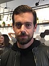 image of Jack Dorsey at a London cafe in November 2014, smiling with his mouth closed, and wearing a dark upper garment and jacket