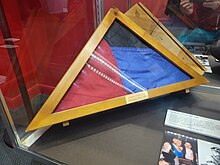 red, blue, and black flag folded within a triangular storage case.