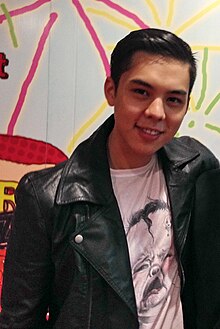 Candid photo of Pachara Chirathivat at VERY TV, wearing a black leather jacket, white t-shirt, and black hair brushed to his right.