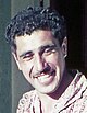 close up head shot of a smiling young man with dark curly hair and a moustache