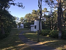 Photo showing the 3 Sisters lighthouses in their new position among the trees and down a winding path away from the coastline. There are 3 similar lighthouses with the beacon in the middle.