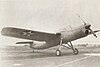 An inline-engined aircraft on tall taildragger landing gear with a mid-wing and 1930s U.S. military insignia