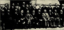 Black and white photo including two rows of middle-aged men wearing dark-coloured suits
