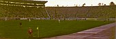 Vue panoramique de l’intérieur d’un stade de football, dans lequel un match se dispute devant des tribunes pleines.